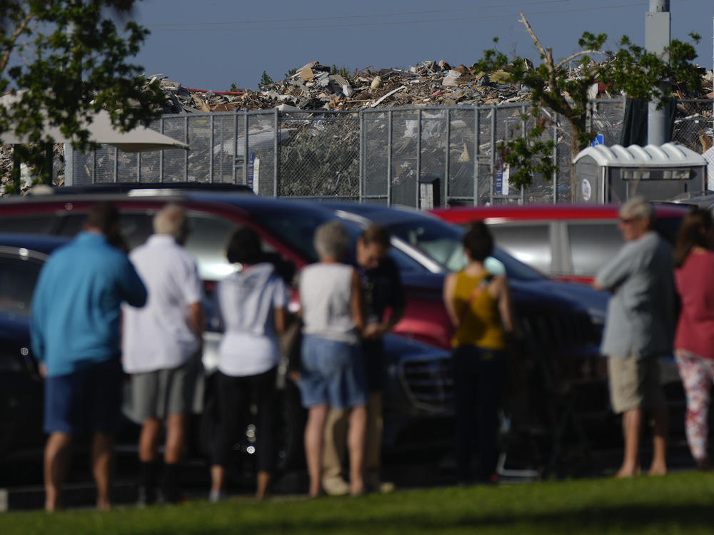 A pile of debris from Hurricane Ian rises behind a line of people waiting to vote in Fort Myers, Fla., in November 2022. Research suggests support for some climate policies increases immediately after climate-driven disasters such as Ian.