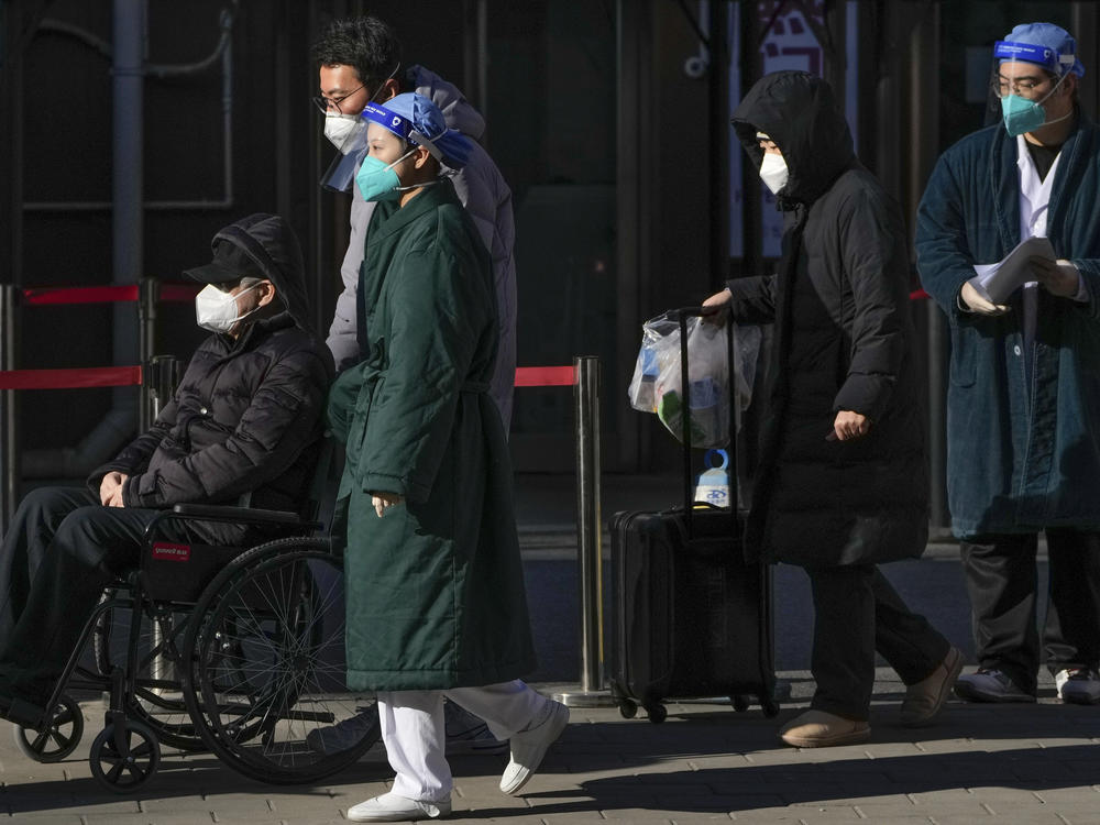 Medical workers in protective gear escort an elderly patient on a wheelchair followed by family members as they leave a fever clinic at a hospital in Beijing on Monday, Dec. 19, 2022.