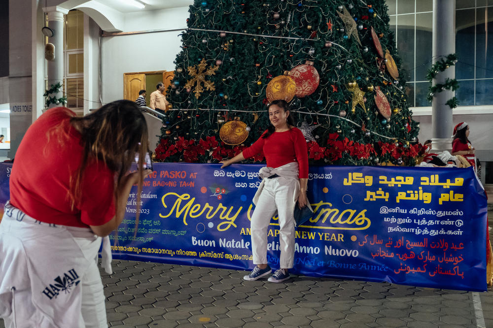 Mai Lumapac stands in front of a large Christmas tree near St. Mary's Catholic Church. She has worked as an administrative assistant in the UAE for over a decade.