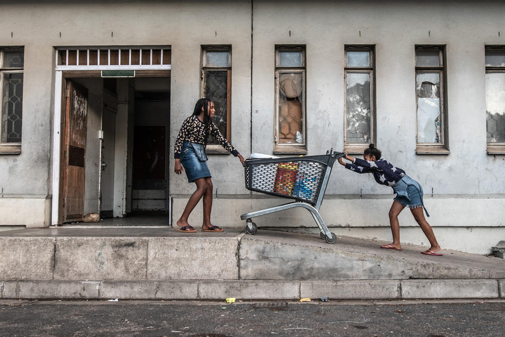 Two girls push a shopping cart full of buckets of water to their families' rooms in Ahmed Kathrada House.