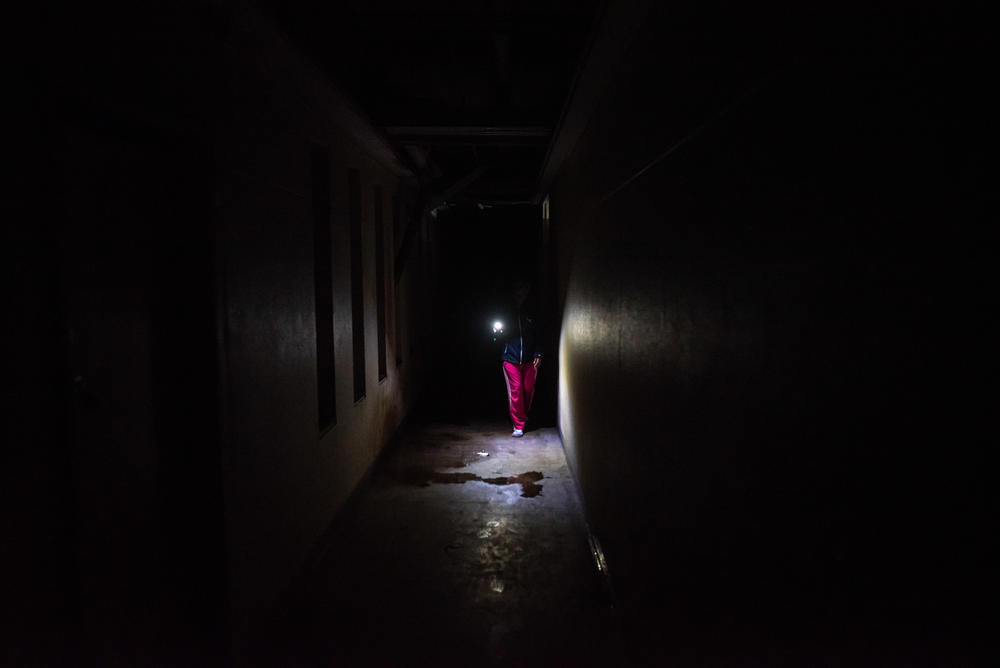 A resident uses a flashlight to navigate along a dark corridor in Ahmed Kathrada House.