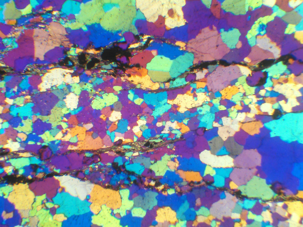 A thin, polished slice of a rock collected from the Jack Hills of Western Australia, viewed through a special microscope equipped with a gypsum plate that shows the rainbow spectrum of quartz that makes up the rock. Whereas the rocks at the Jack Hills are greater than 99% quartz, the remaining 1% of material includes the precious zircons.