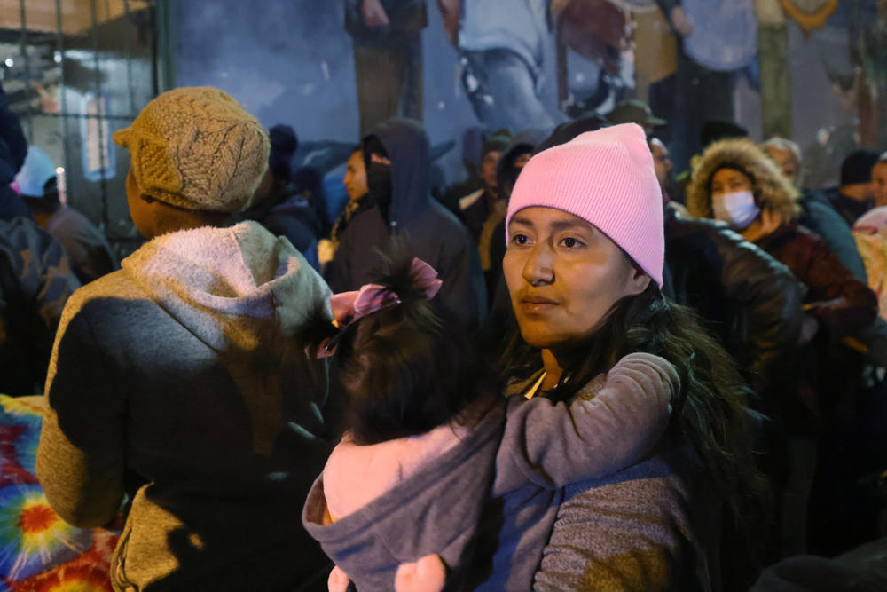 An unsheltered migrant from Peru holds her daughter as they wait for bed space to open for the evening in the gymnasium at Sacred Heart Church.