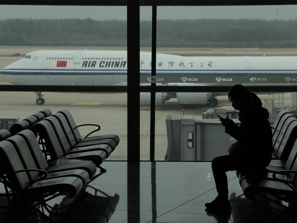 A passenger checks her phone as an Air China passenger jet taxis past at the Beijing Capital International airport on Oct. 29. China will drop a COVID-19 quarantine requirement for passengers arriving from abroad starting Jan. 8.