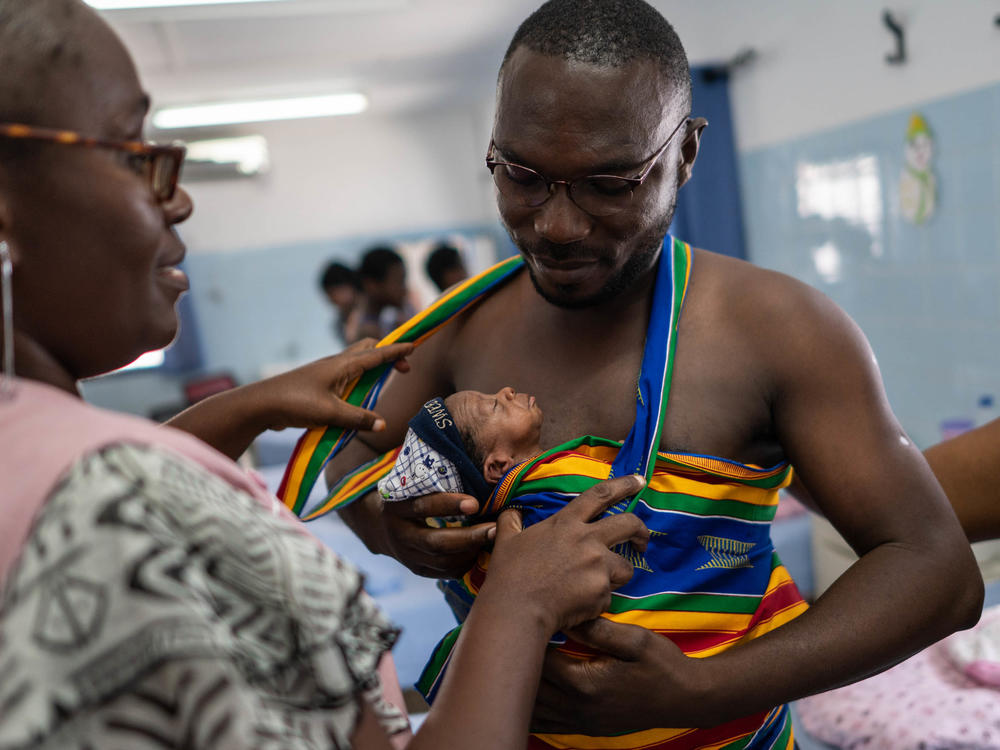 New father Yappe Pako gets help with his kangaroo care carrier from a midwife. His newborn son is named Ambo Crisostome. They're in the kangaroo care ward at the University Hospital Medical Center at Treichville in the Ivory Coast. A new program teaches the technique to moms and dads. It's especially beneficial for preterm and low birthweight babies.