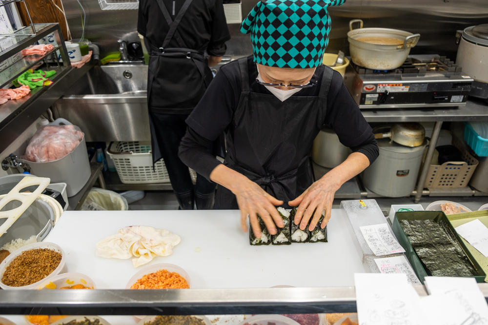 Onigiri Bongo owner Yumiko Ukon wraps triangular rice balls in thin sheets of nori, or dried seaweed, behind the counter at her restaurant.