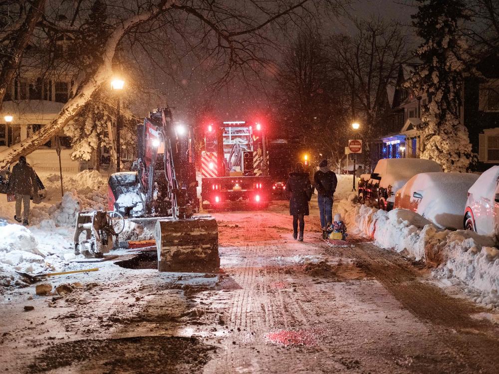 Pedestrians walk past workers attempting to repair a water line in Buffalo on Monday.