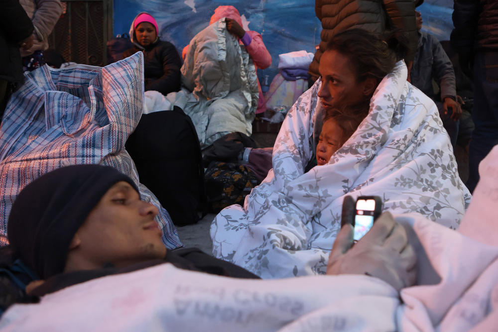 An unsheltered migrant family from Venezuela lays covered in blankets on the sidewalk in front of Sacred Heart Church on Wednesday.