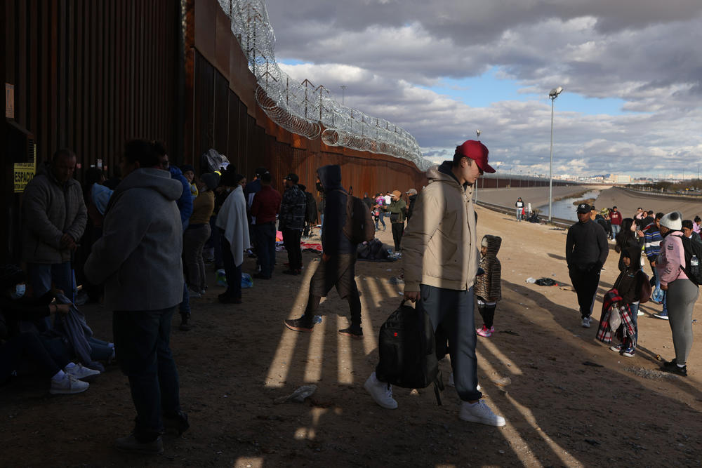 Migrants wait to be escorted around the border wall to be processed by U.S. Customs and Border Protection after crossing the Rio Grande River into the United States in El Paso, Texas, U.S., Dec. 30, 2022.