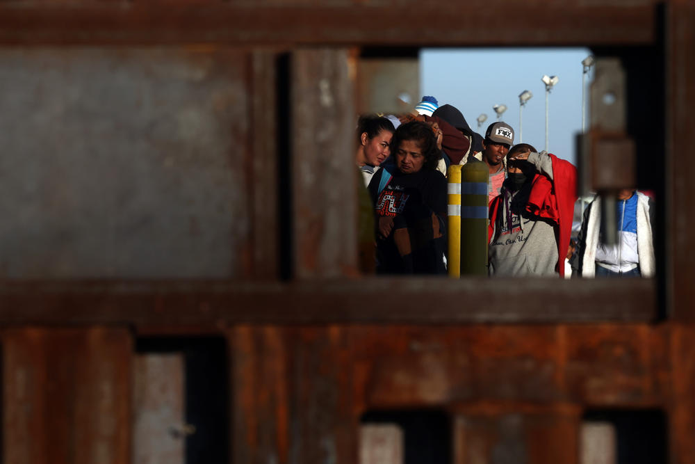 Migrants wait at the border wall to be processed by U.S. Customs and Border Protection on Dec. 21 after crossing the Rio Grande.