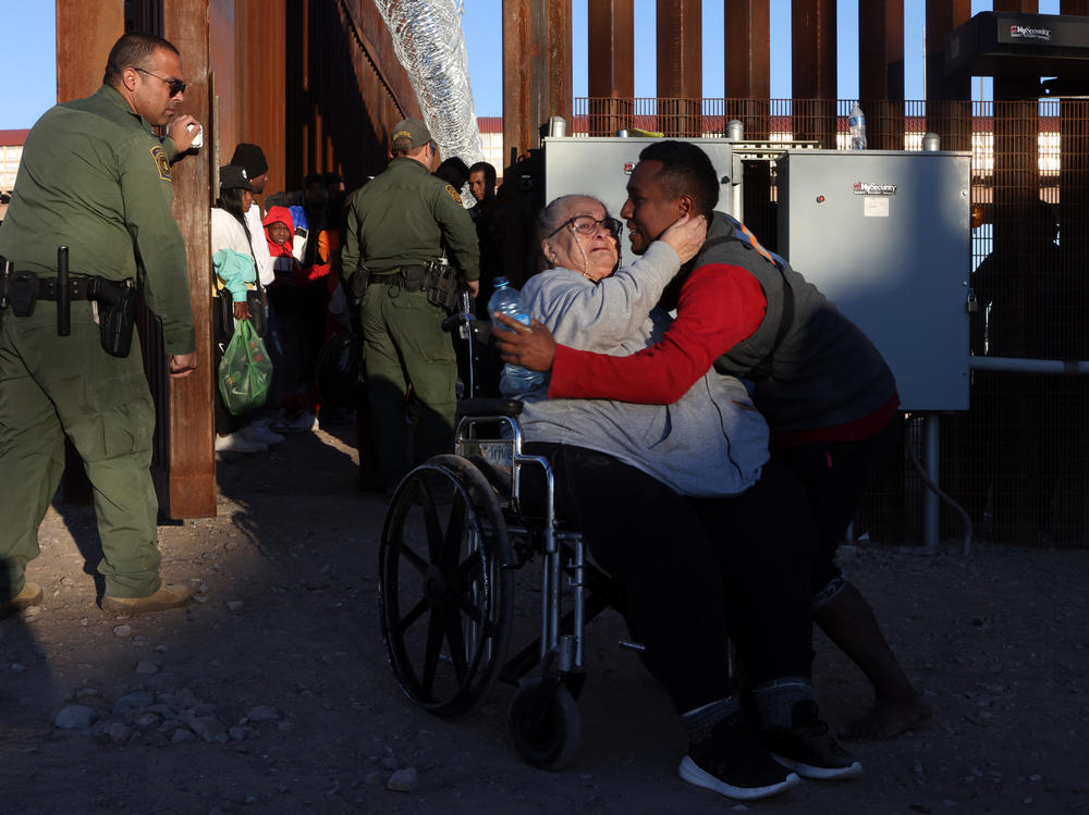 An asylum-seeking migrant woman from Peru in a wheelchair is escorted through the border wall to be processed by U.S. Customs and Border Protection after crossing the Rio Grande into the United States in El Paso, Texas, on Dec. 21.