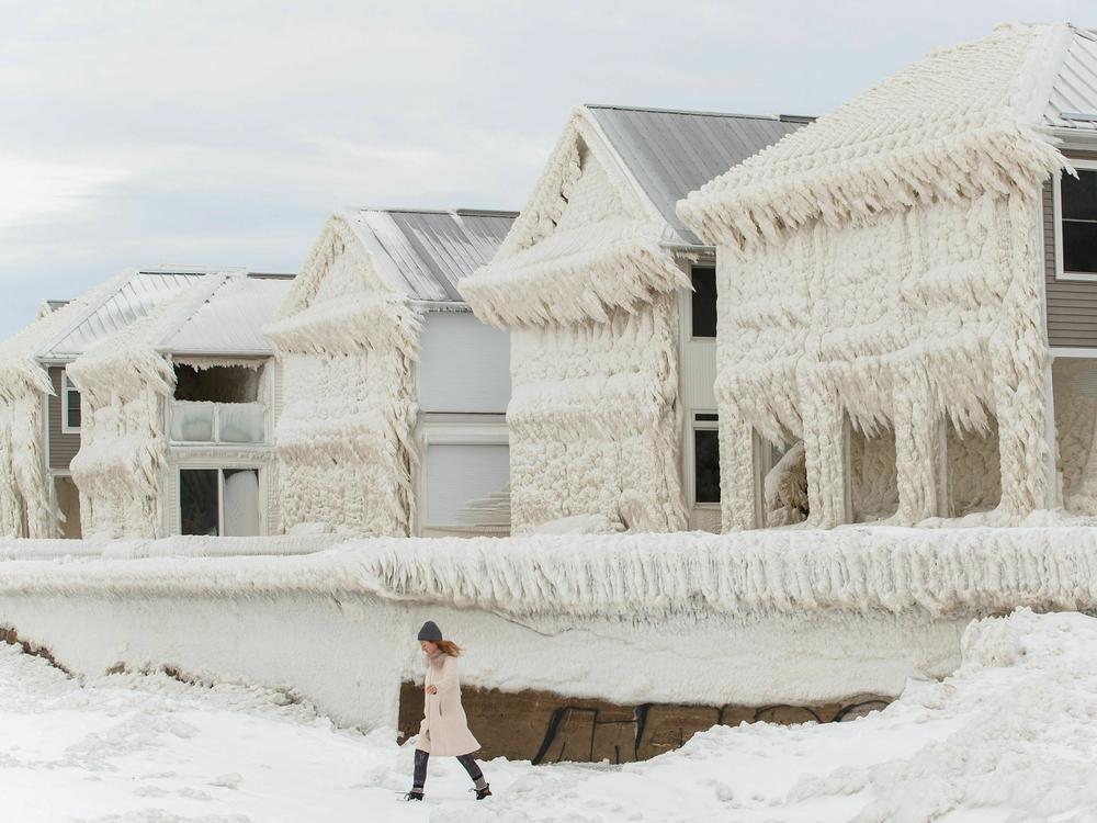 A person walks by homes covered in ice at the waterfront community of Crystal Beach in Fort Erie, Ontario, Canada, on Wednesday, following a massive snowstorm that knocked out power in the area to thousands of residents.