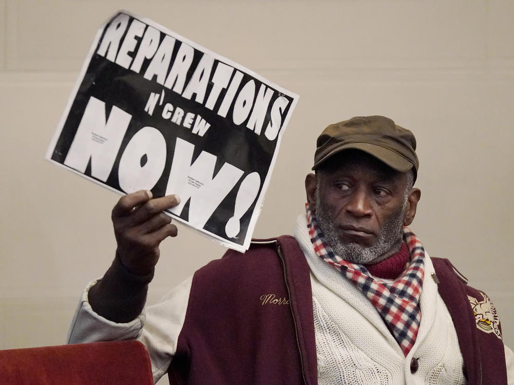 Globally, attitudes toward reparations are changing, experts say. Morris Griffin (pictured) holds up a sign during a meeting by the Task Force to Study and Develop Reparation Proposals for African Americans in Oakland, Calif.