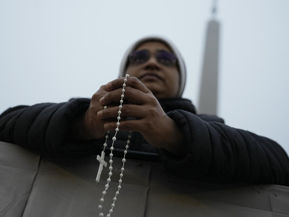 A woman holds a cross as she waits the funeral mass for late Pope Emeritus Benedict XVI, in St. Peter's Square at the Vatican, Thursday, Jan. 5, 2023.