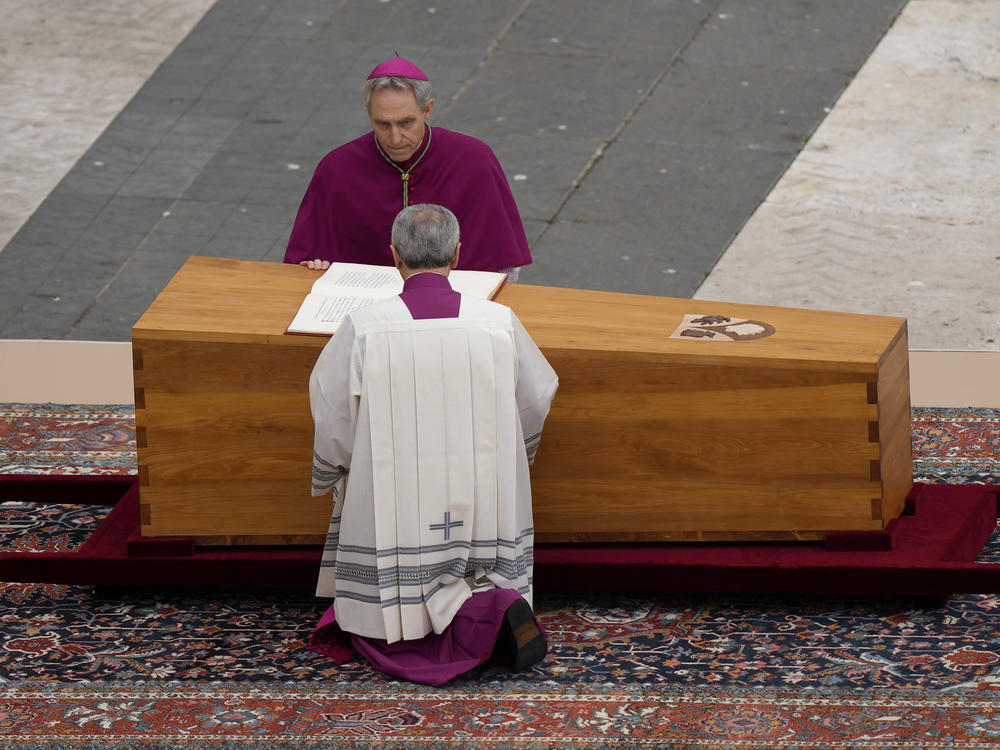 Archbishop Georg Ganswein kneels by the coffin of late Pope Emeritus Benedict XVI is brought to St. Peter's Square for a funeral mass at the Vatican, Thursday, Jan. 5, 2023.