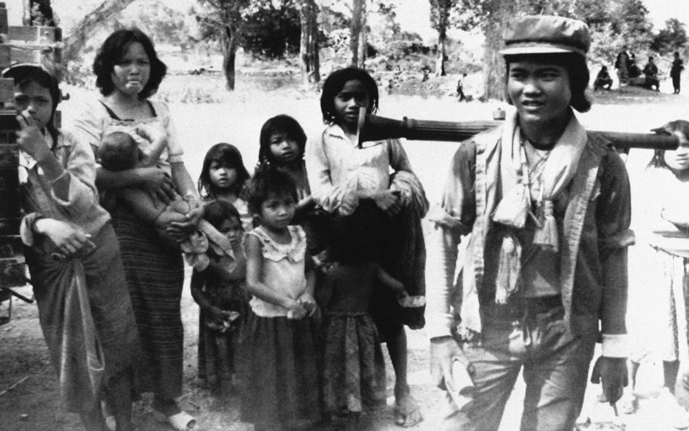 In this 1990 photo taken by Thayer, a Khmer Rouge guerrilla with a rocket-propelled grenade launcher strapped to his back and Buddhist amulets on his neck passes by villagers on his way to the front in Banteay Meanchey province, Cambodia.