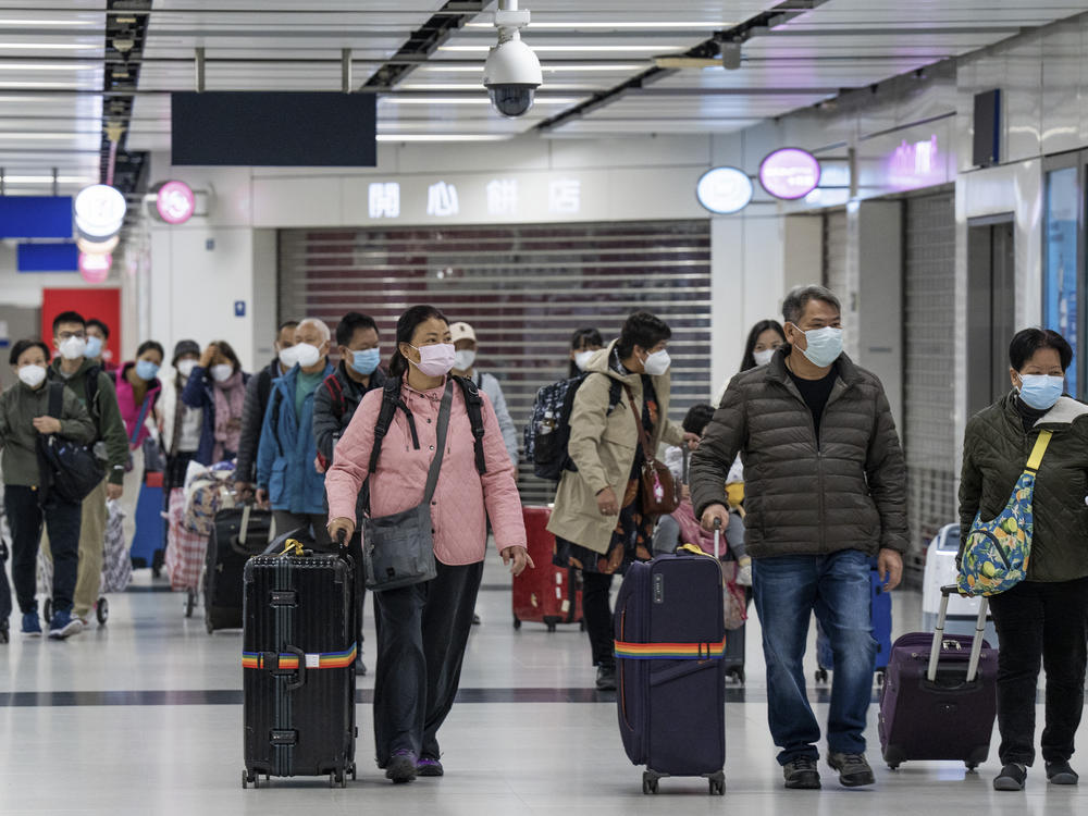 Travelers wearing face masks with their luggage head to the immigration counter at the departure hall at Lok Ma Chau station following the reopening of crossing border with mainland China, in Hong Kong, Sunday, Jan. 8, 2023.