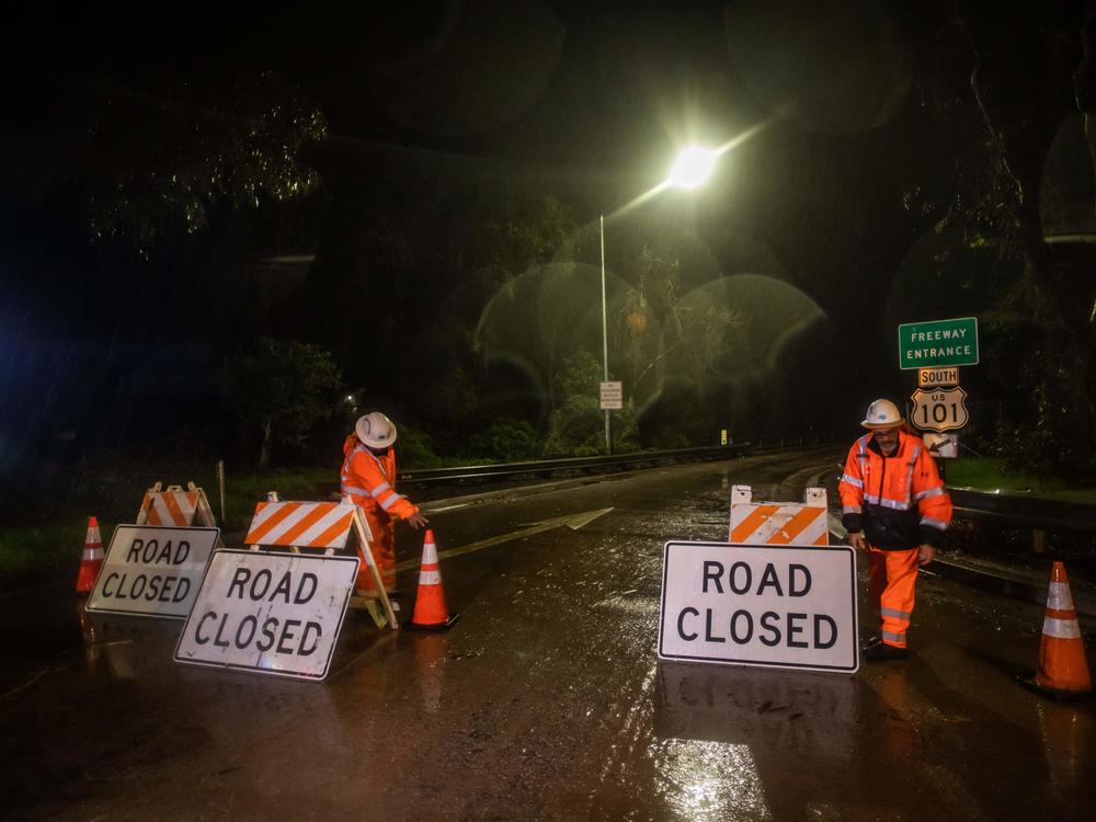 Road workers close access to the 101 Freeway as a result of the San Ysidro Creek overflowing due to heavy rainfall in the area Monday.