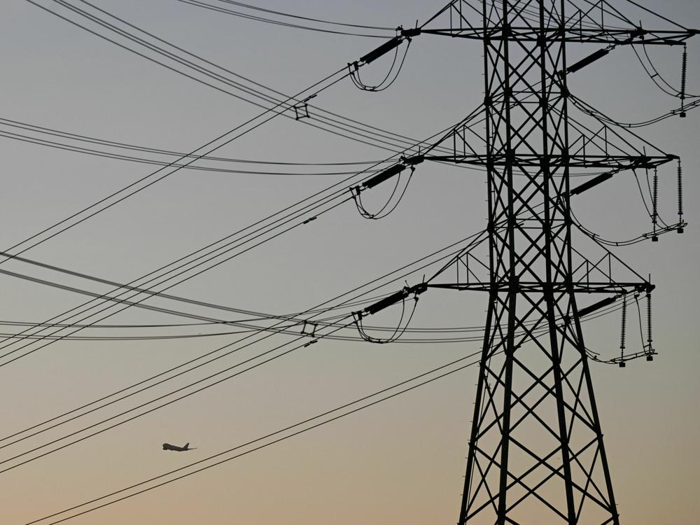 An aircraft takes off from Los Angeles International Airport behind electric power lines at sunset.