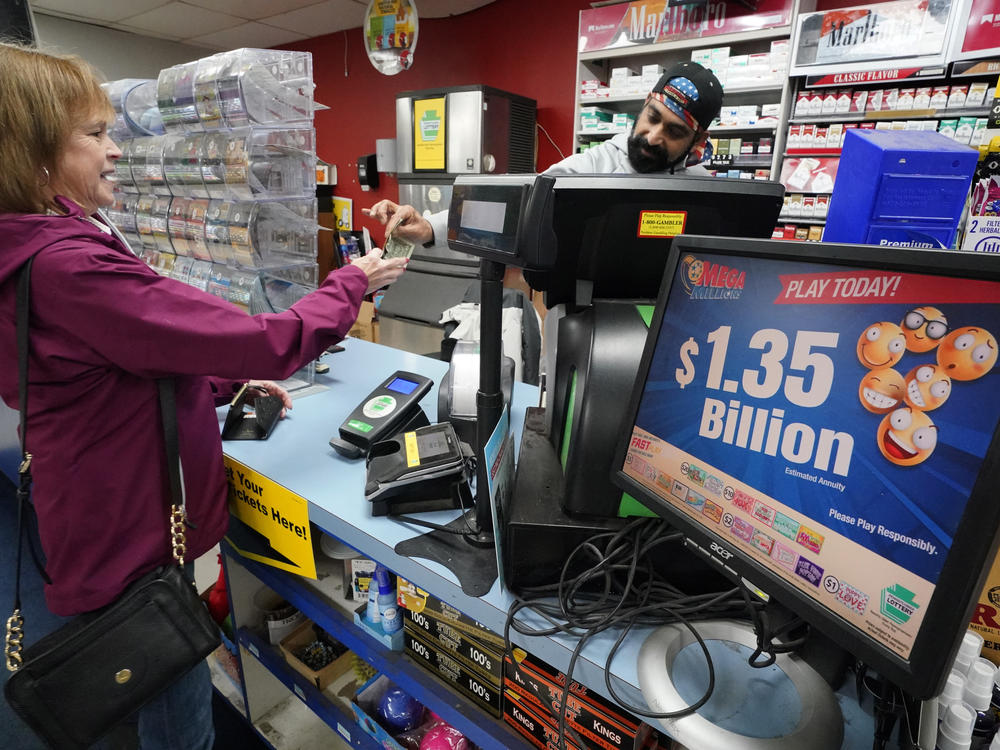 A Mega Millions sign displays the estimated jackpot of $1.35 billion as a customer purchases a ticket at the Cranberry Super Mini Mart in Cranberry, Pa., on Jan. 12, 2023.