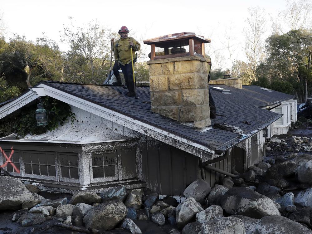 A firefighter stands on the roof of a house submerged in mud and rocks, Jan. 10, 2018, in Montecito, Calif.