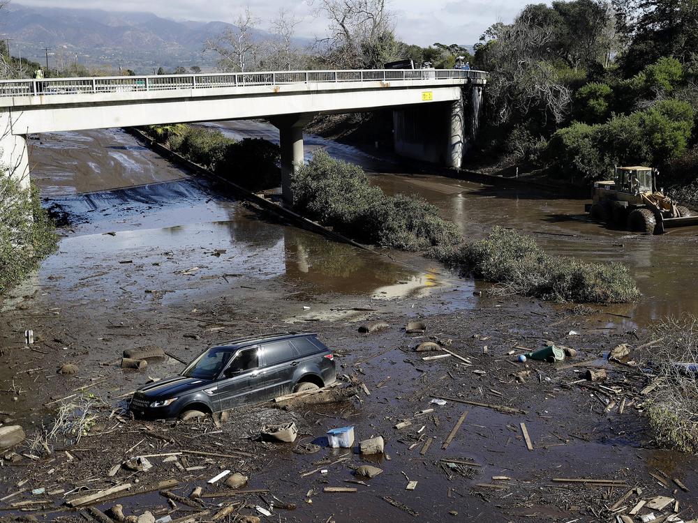 A bulldozer moves debris as a vehicle sits stranded in flooded water on U.S. Highway 101 in Montecito, Calif., Jan. 10, 2018.