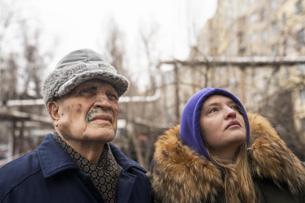Petro Shevchenko, (left) stands with his grandaughter, Olena Parkhomenko, as they look at the damaged apartment building. Shevchenko, 85, lives alone on the 7th floor and has cuts on his face from the attack.
