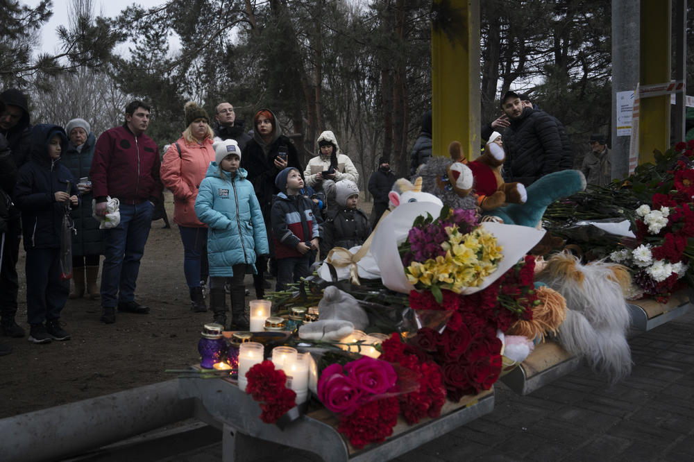 Flowers, candles, and stuffed animals are piled on the seat of a bus stop across the street from where the crews continue to search the apartment building.