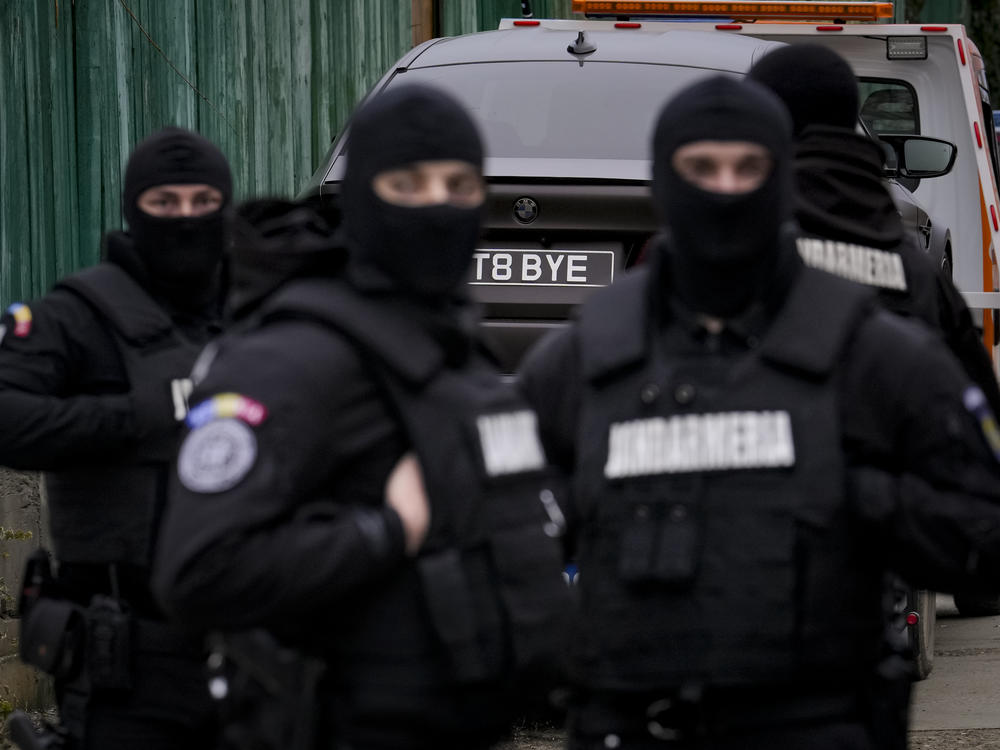 Romanian officials are backdropped by a luxury vehicle that was seized in a case against media influencer Andrew Tate on Saturday.