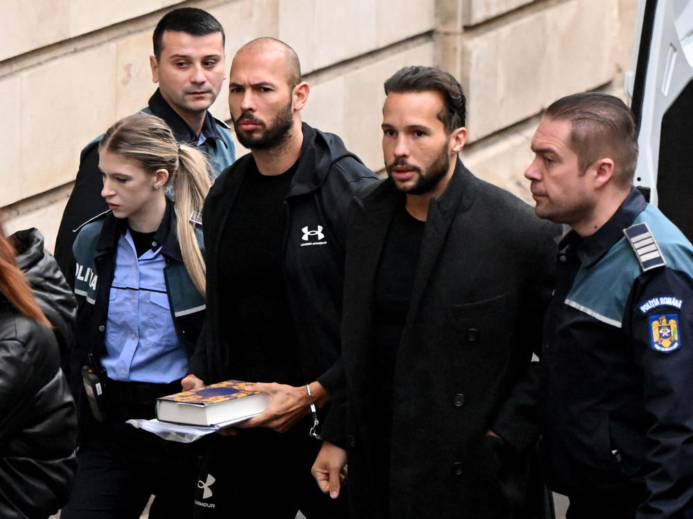 Andrew Tate (pictured third from the right) and his brother Tristan Tate (second from the right) arrive handcuffed and escorted by police at a courthouse in Bucharest on Jan. 10 for a hearing on their appeal against pretrial detention for alleged human trafficking, rape and forming a criminal group.