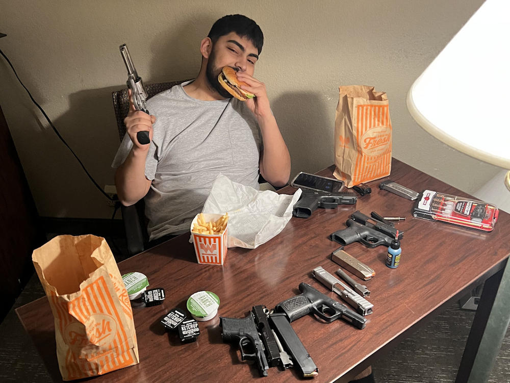 A photo that police say was sent from the phone of Solomon Peña shows José Trujillo eating a hamburger while holding a pistol. Trujillo and others are named in a criminal complaint charging Peña with orchestrating a string of shootings.
