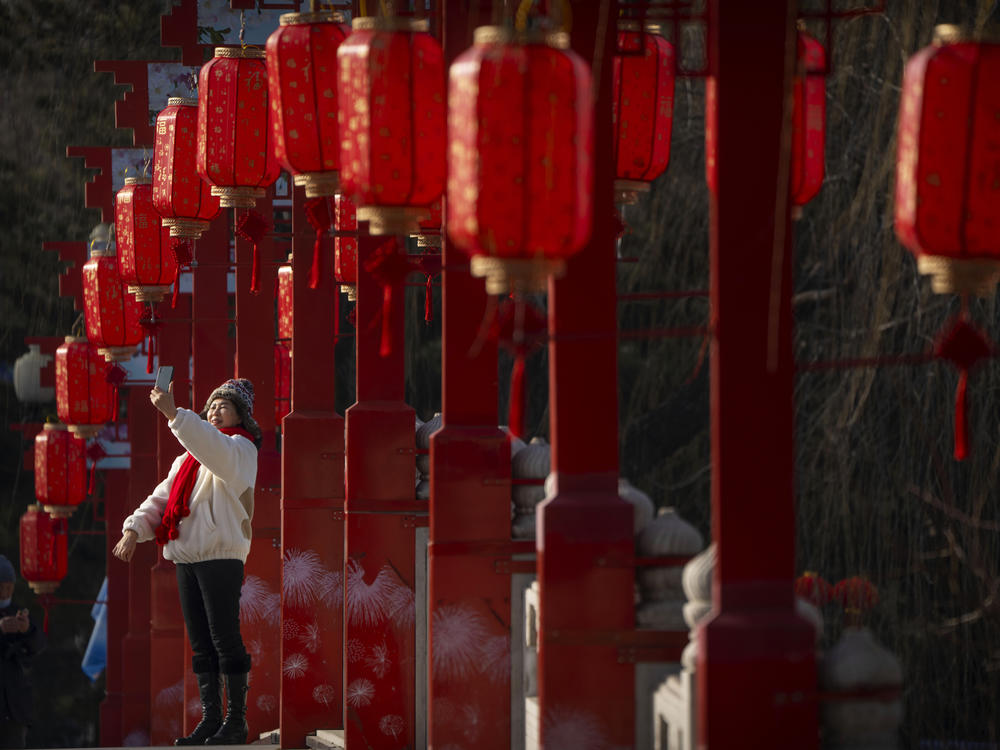 A woman poses for a selfie on a bridge decorated with lanterns at a public park in Beijing on the first day of the Lunar New Year holiday, Sunday, Jan. 22, 2023.