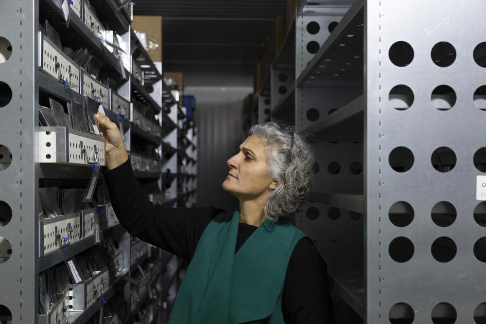 Mariana Yazbek, the seed bank manager, holds a sealed foil packet containing seed samples as she stands between two rows of heavy sliding metal shelves in the large freezer room where the seeds are stored at the ICARDA research station.