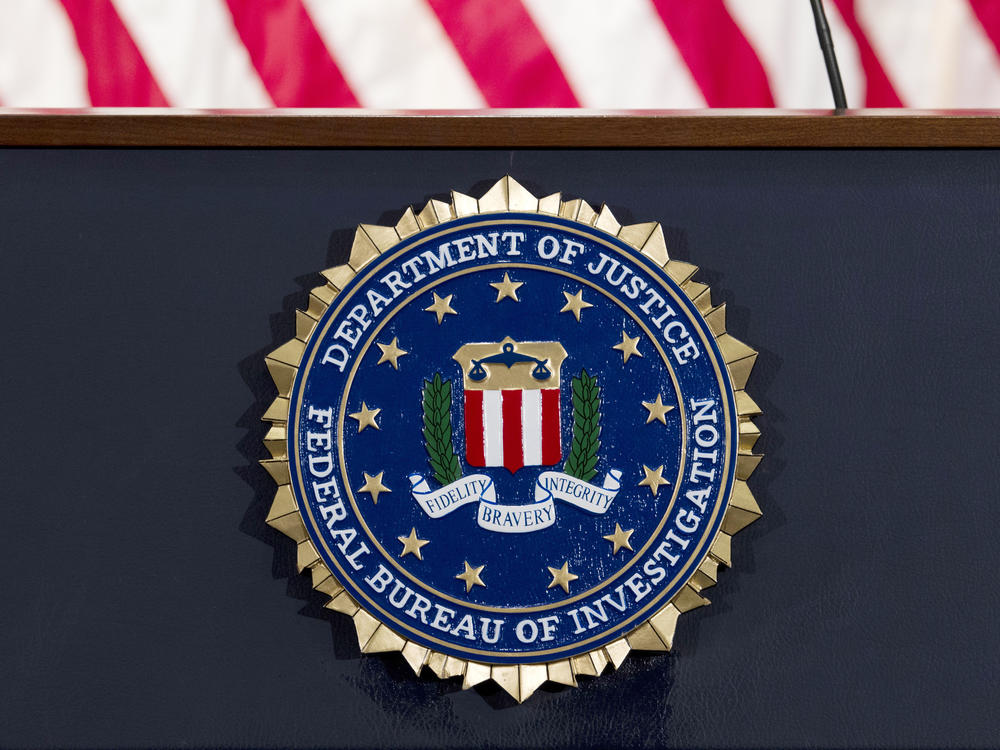 The FBI seal is displayed on a podium. A former FBI agent is facing several charges tied to his work with a Russian oligarch.