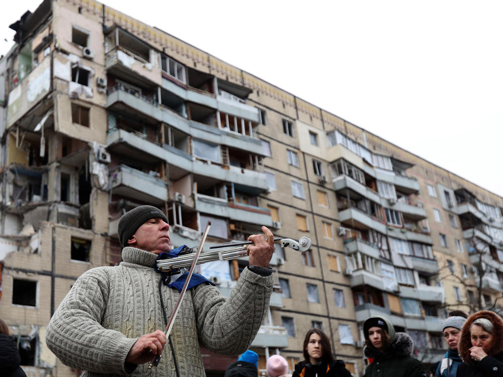 A man plays violin on the sidelines of a religious service held by local residents in front of an apartment building in the Ukrainian city of Dnipro on Sunday. The building was destroyed by a Russian missile strike on Jan. 14.