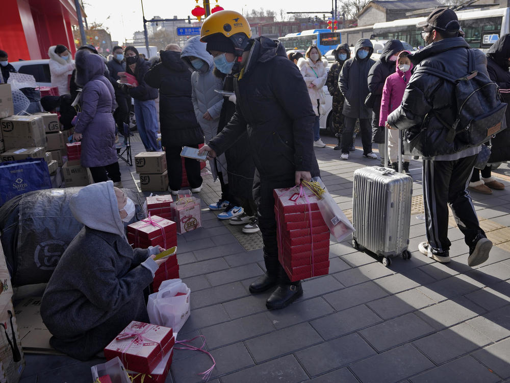A delivery rider picks up his customers' online order as residents line up outside a store to buy Lunar New Year desserts in Beijing, Jan. 17. China's economic growth fell to its second-lowest level in at least four decades last year under pressure from anti-virus controls and a real estate slump.