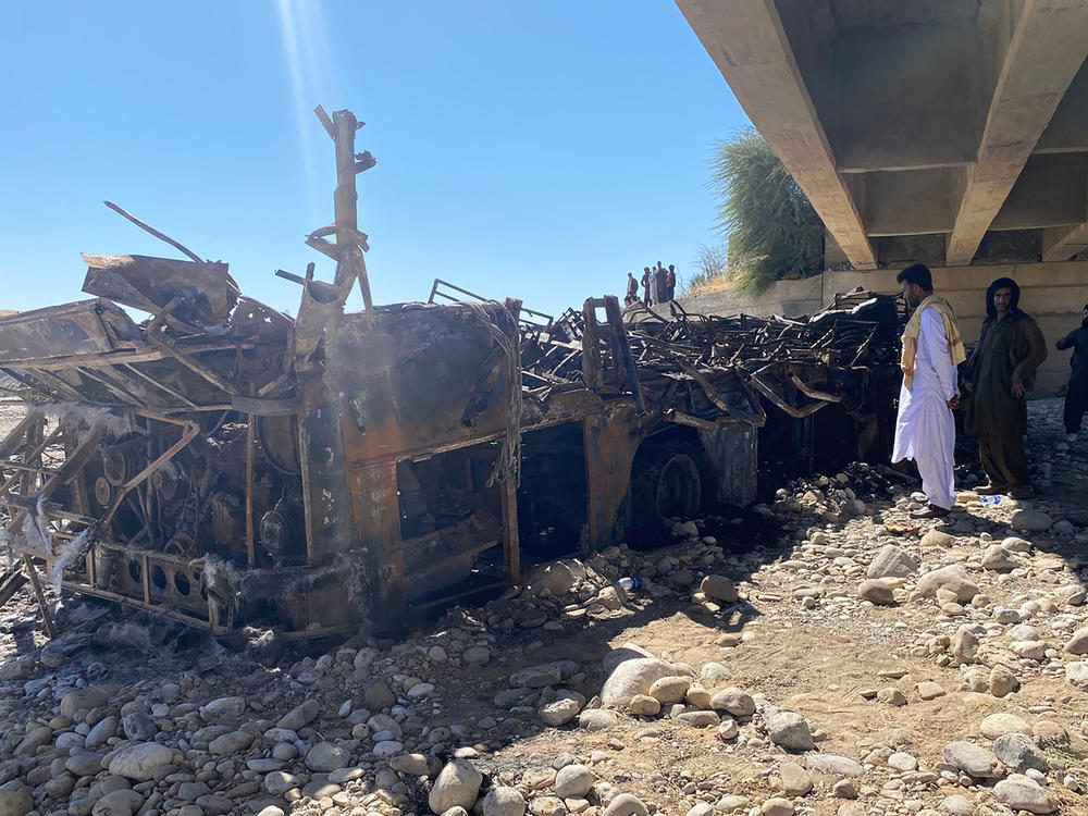 People look at the burnt wreckage of a bus in Bela, an area of Lasbela district of Balochistan province, Pakistan, on Sunday. The passenger bus crashed into a pillar and fell off a bridge, catching fire and killing dozens of people.