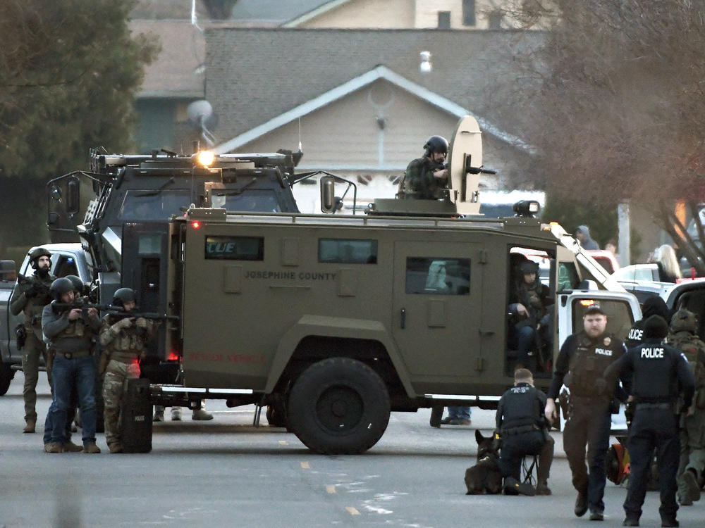 Law enforcement officers aim their weapons at a home during a standoff in Grants Pass, Ore., on Tuesday, Jan. 31, 2023. Police said the standoff involving a man suspected in a violent kidnapping in Oregon who was barricaded underneath the home had been 