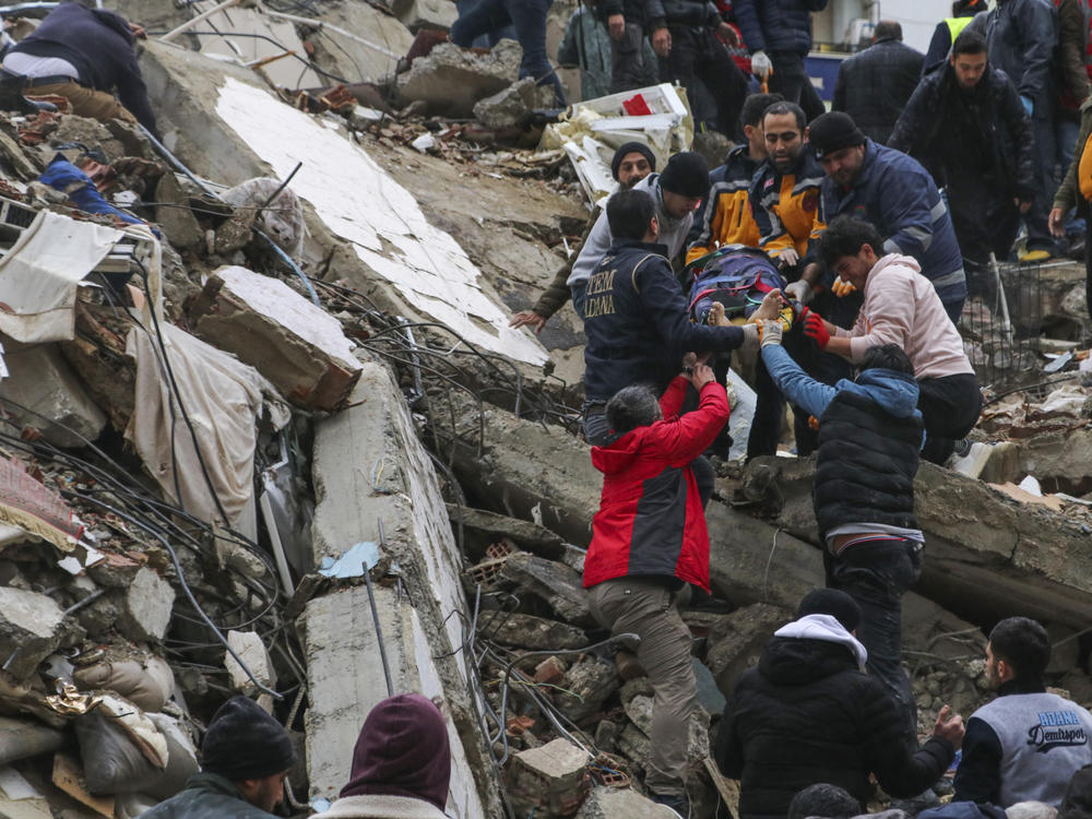 People and emergency teams rescue a person on a stretcher from a collapsed building in Adana, Turkey, Monday, Feb. 6, 2023.