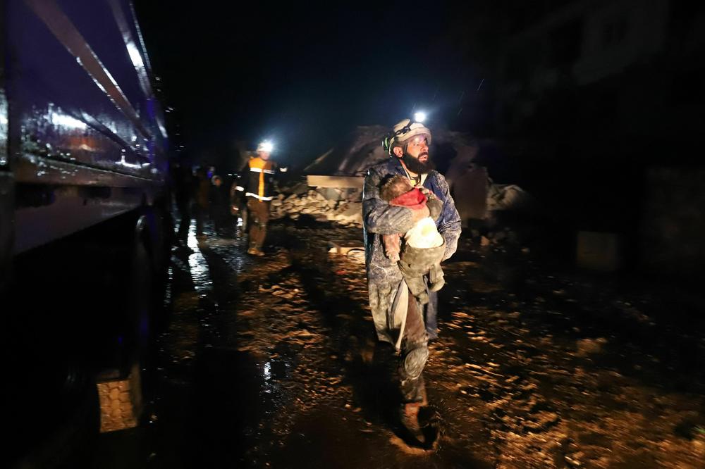 A member of the Syrian civil defense, known as the White Helmets, carries a child rescued from the rubble following an earthquake in the town of Zardana in the countryside of the northwestern Syrian Idlib province, early on Monday.