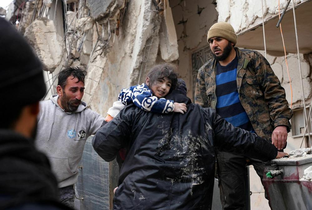 Residents retrieve a child from the rubble of a collapsed building following an earthquake in the town of Jandaris, Syria.