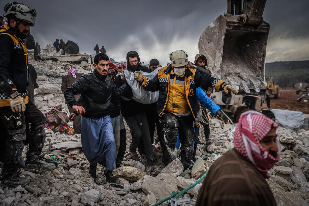 Syrian civilians and members of the White Helmets conduct search and rescue operations in the rubble of a collapsed building.