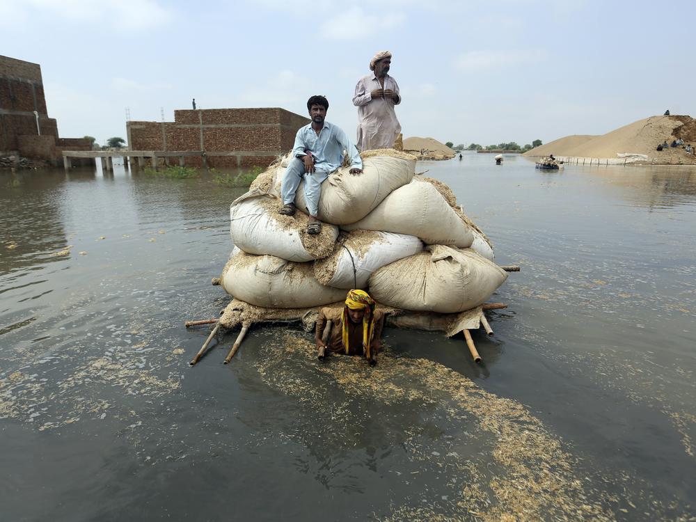 Residents of southwest Pakistan move through floodwaters in September 2022. People with less wealth are more vulnerable to the effects of climate change, including more severe rainstorms.