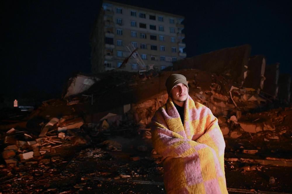 A man looks at rescue personnel searching for victims and survivors through the rubble of buildings in Kahramanmaras, Turkey after a 7.8-magnitude earthquake struck the country's southeast.