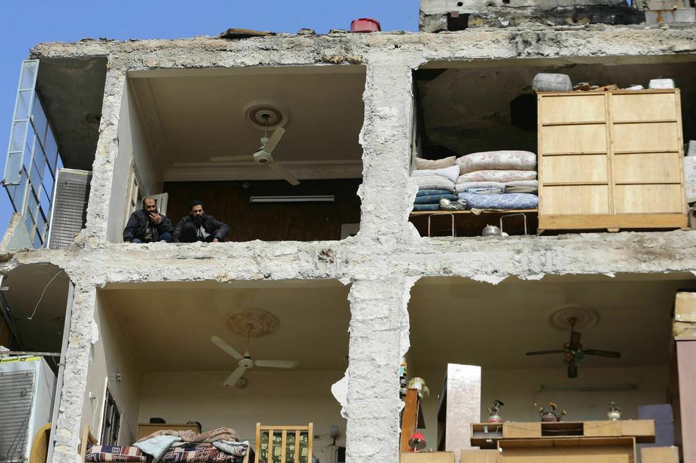 Two men watch from the top floor of a damaged building as rescue teams search for victims and survivors stuck under the rubble in the government-held northern Syrian city of Aleppo on Tuesday, following a deadly earthquake that hit the region the previous day.