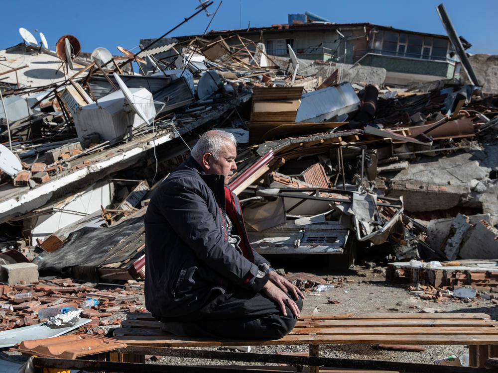 A man prays in front of a collapsed building in Hatay, Turkey.