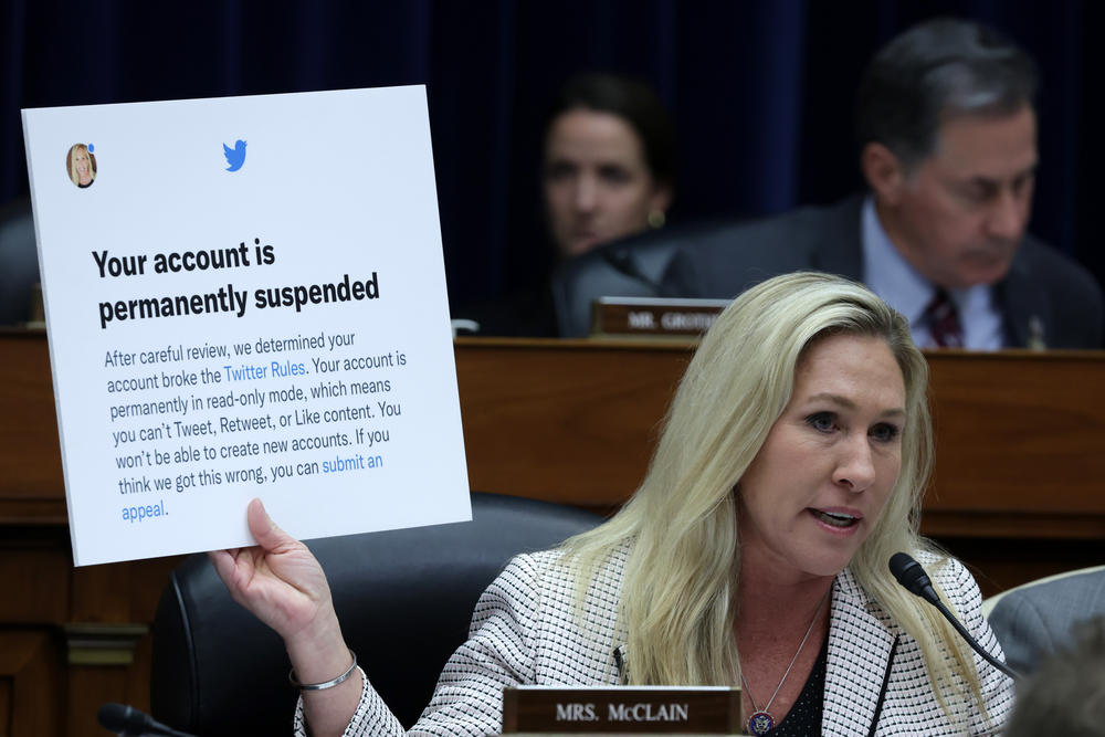 Rep. Marjorie Taylor-Greene, R-Ga., holds up a poster of a Twitter announcement of suspending her account during the House Oversight Committee hearing.