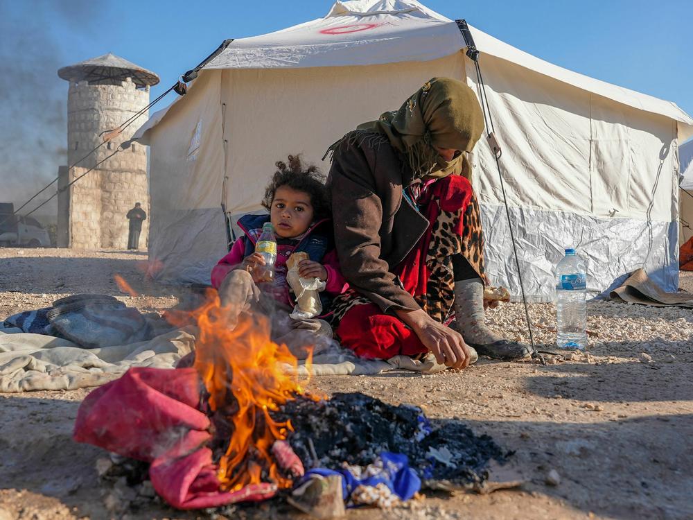 Syrians warm up by a fire at a make-shift shelter for people who were left homeless, near the rebel-held town of Jindayris on Feb. 8, 2023.