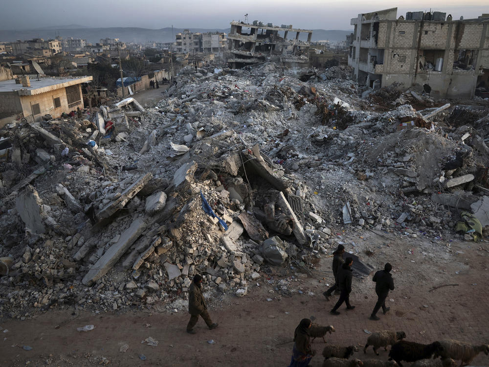 People walk past collapsed buildings on Thursday in the town of Jinderis, in Syria's Aleppo province, days after a massive earthquake devastated the region.