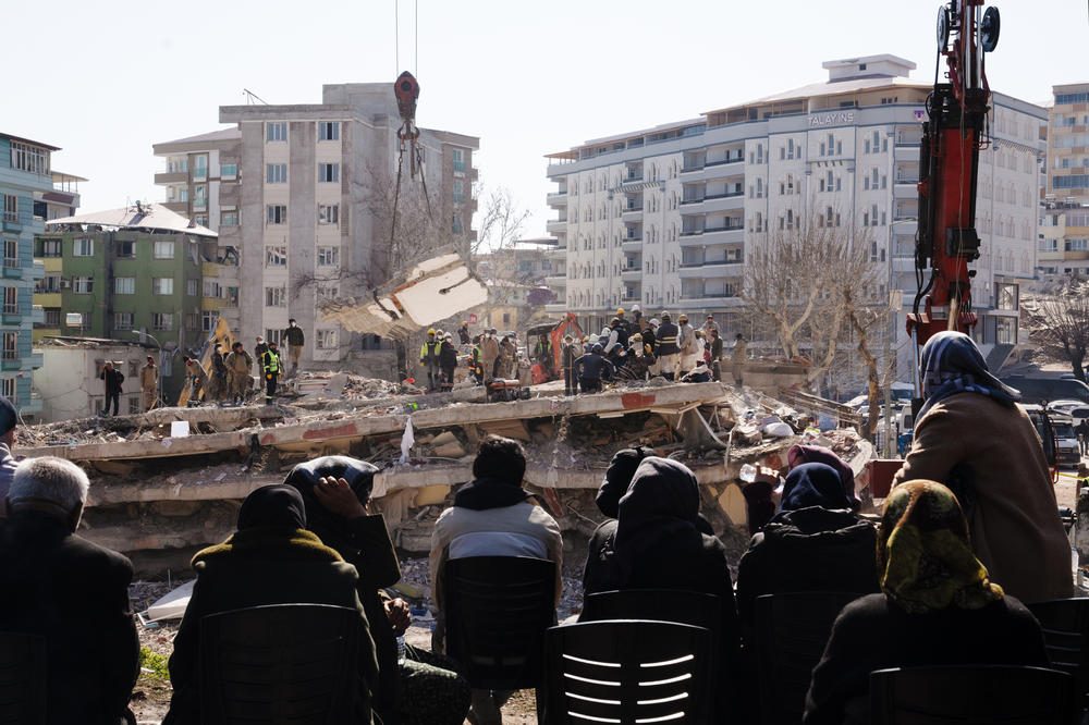 People watch as workers dig through a collapsed apartment building, looking for people who were inside the building when it collapsed in Islahiye, Turkey, on Sunday. In the week since a magnitude 7.8 earthquake and a series of powerful aftershocks hit Turkey and Syria, leveling cities like Islahiye, over 36,000 people have died.